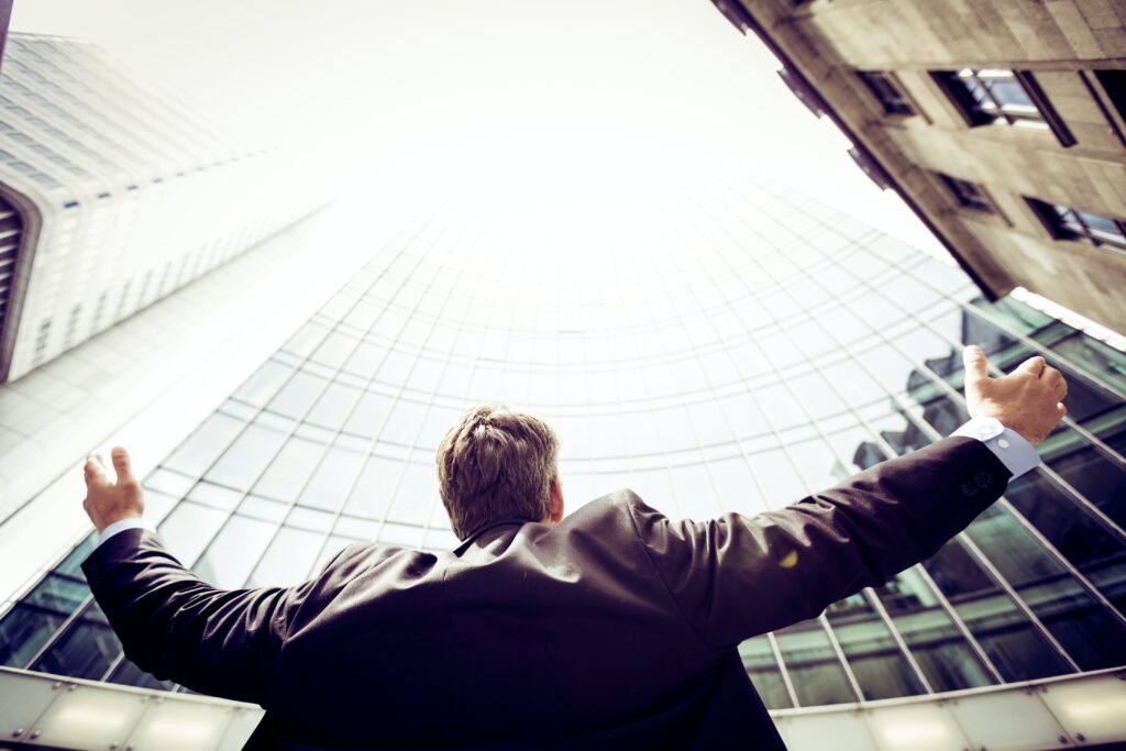 Man in suti with arms outstretched looking up at a skycraper to represent the possibilities that rebranding can bring