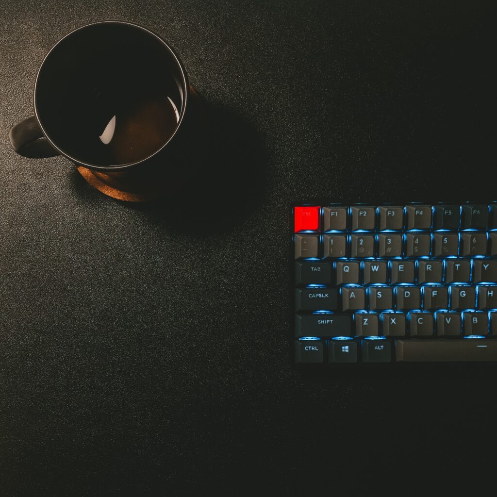 Black keyboard and cup of coffee on a black desk
