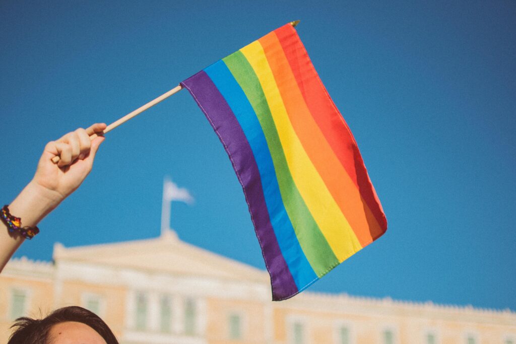 Man holding a Pride flag in the air against a blue sky