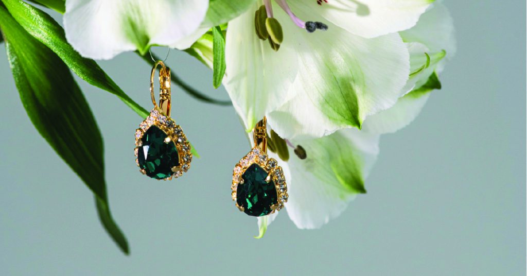 Expensive emerald earrings hanging from the branch of a white flowering plant