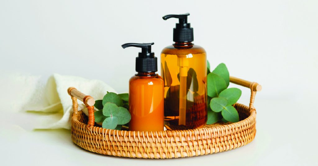 Lifestyle imagery of cosmetics bottles on a rattan tray with green foliage