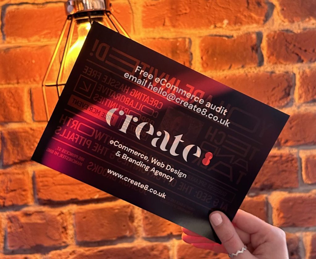 Person holding a flyer against a brick background that reads 'free eCommerce audit with Create8'