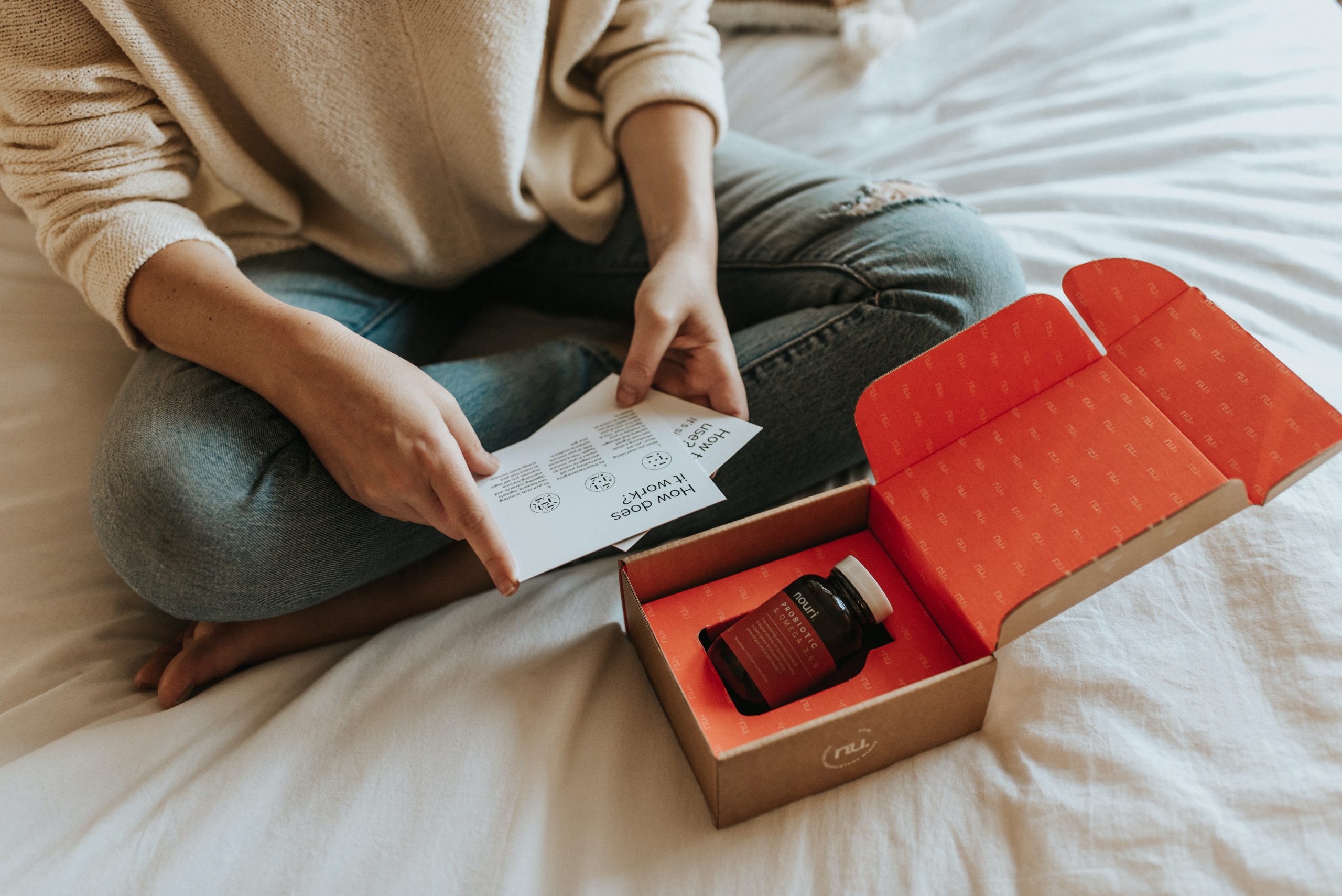 Woman sat on the bed opening an eCommerce delivery package with a red jar inside