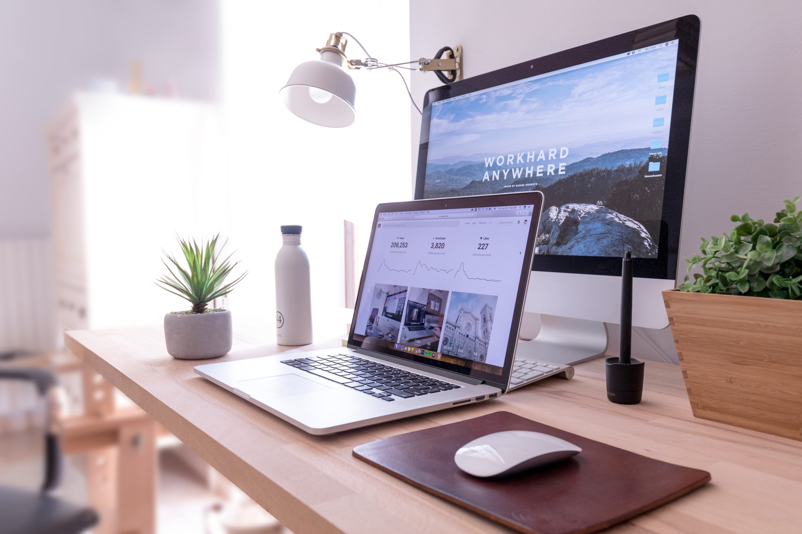 Desktop computer and laptop computer with responsive website design on a wooden desk with a plant and water bottle