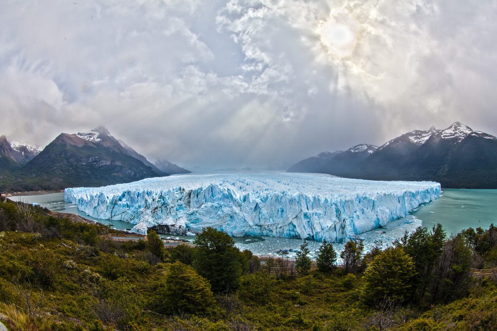 A large frozen glacier surrounded by forests and mountains