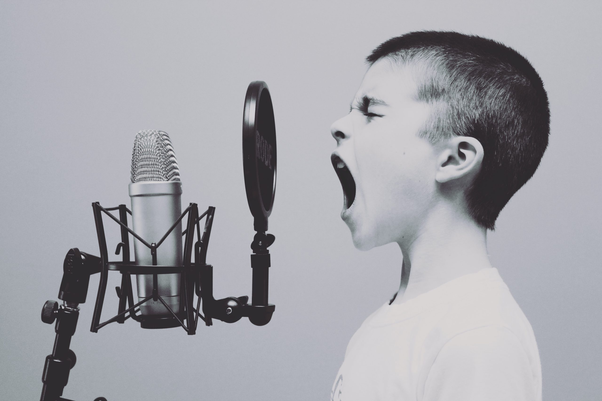 Black and white image of a young boy using his voice to shout into a microphone
