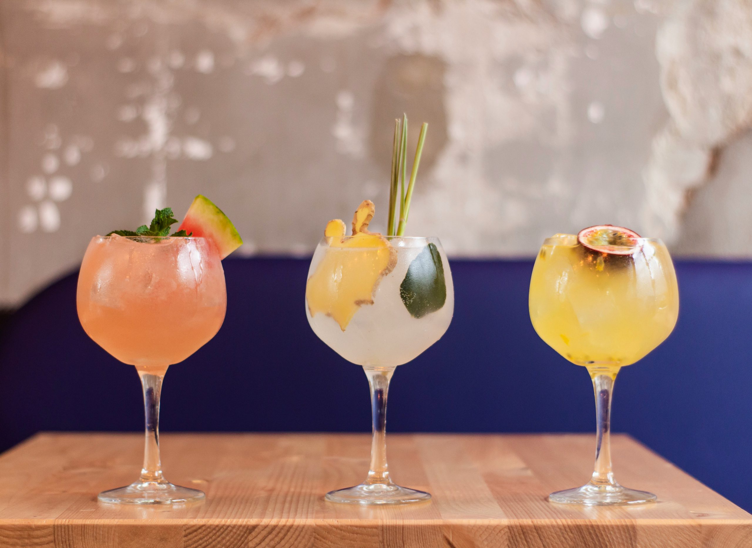three gin glasses on a table with various gin garnishes