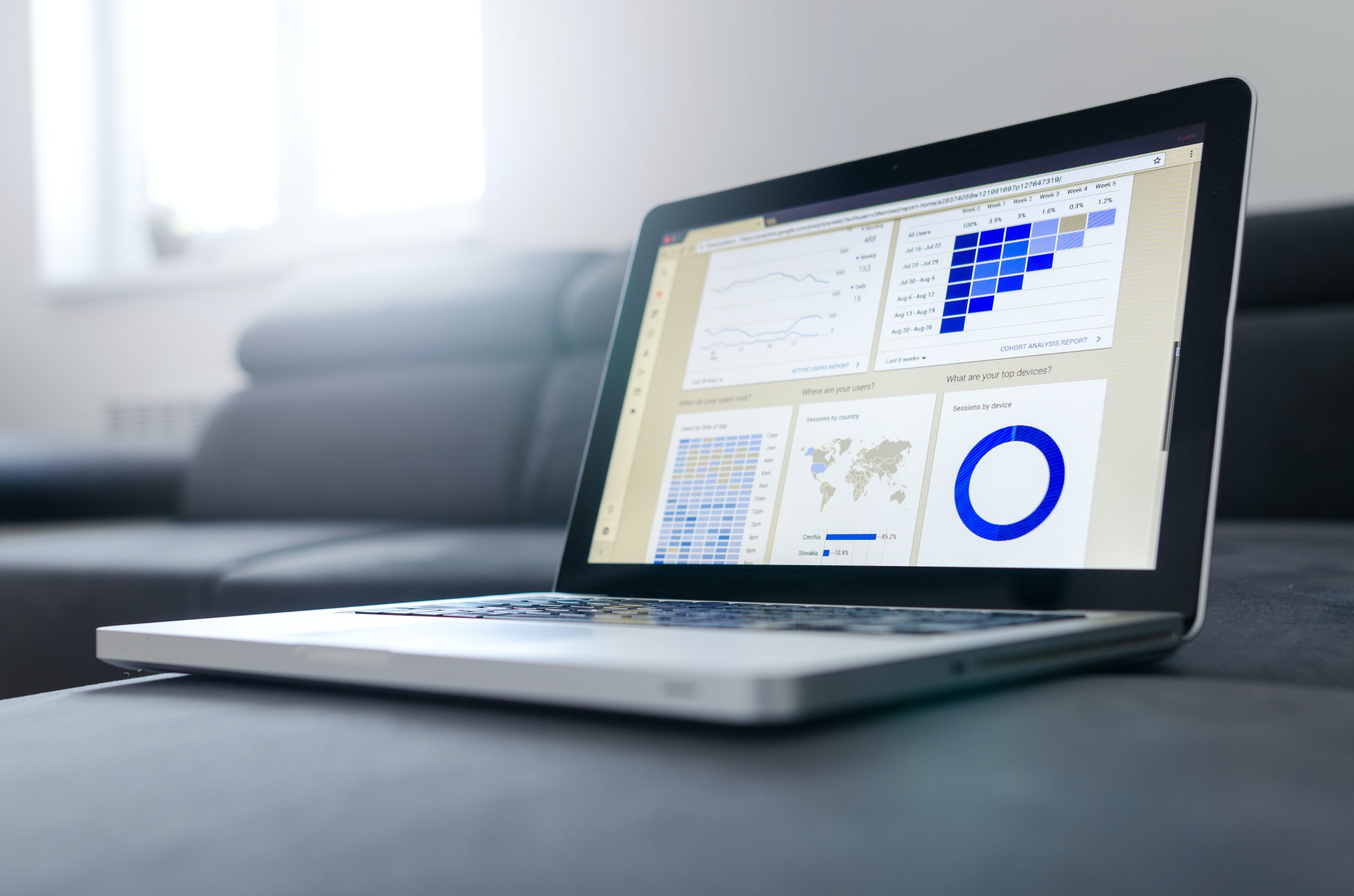A laptop displaying graphs and statistics on a grey coffee table with a sofa in the background