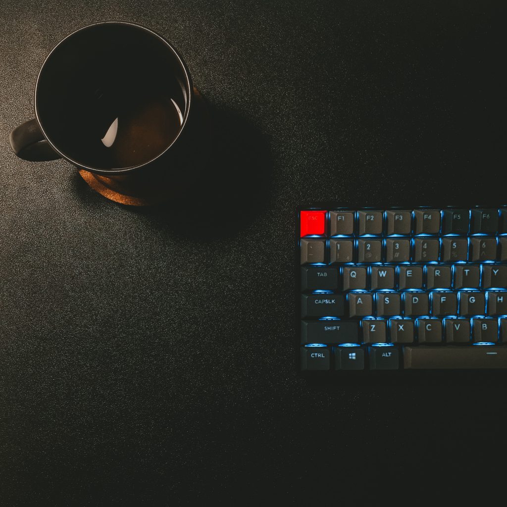 Black keyboard and cup of coffee on a black desk