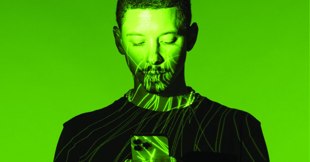 A man against a green background holding a phone and browsing a Shopify store