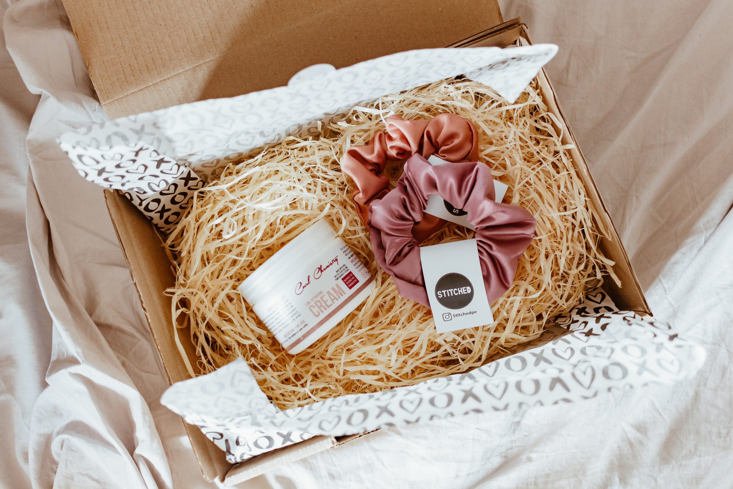 Cardboard beauty subscription box with face cream and hair scrunchies on a bed of straw